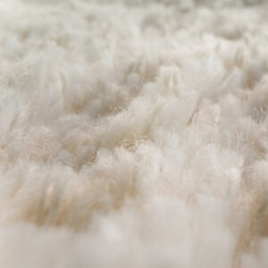 Zbliżenie na miękki, puszysty biały dywan lub chodnik, ukazujące szczegółowo włókna i fakturę, przy niewielkiej głębi ostrości.
