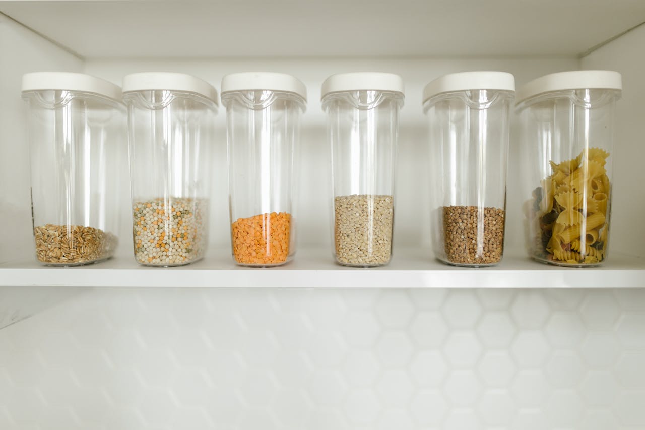 Clear containers filled with grains, pasta, and seeds, neatly organized on a shelf.