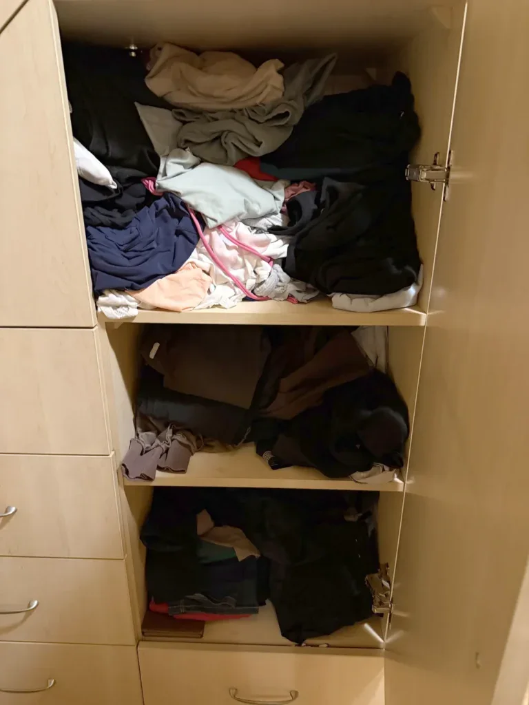Szafa przed declutteringiem, ubrania w wysokich poziomych stertach